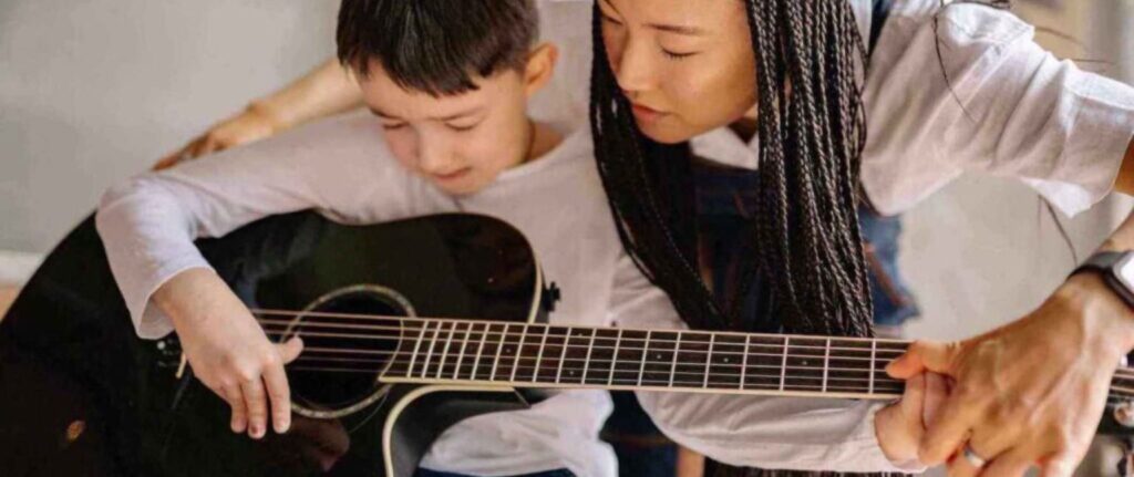 teacher helping student play the guitar