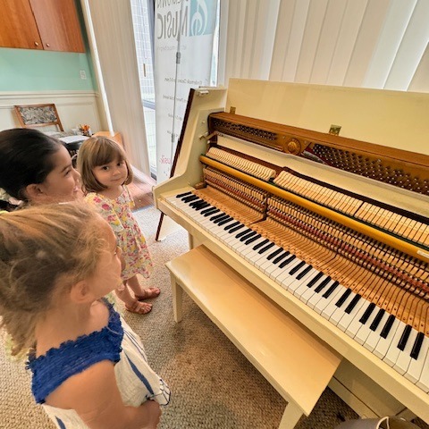 Young toddlers standing around a piano