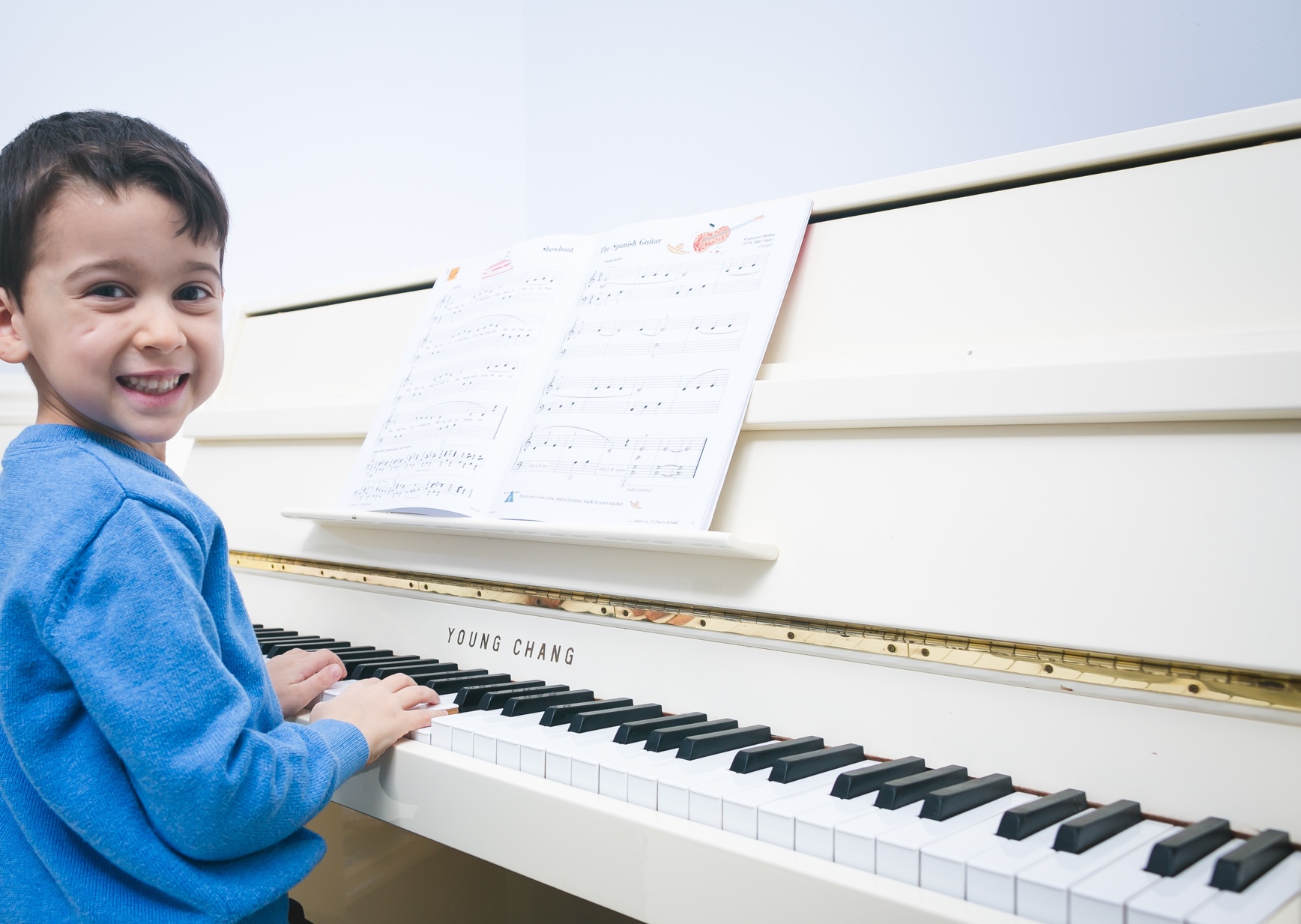 Boy sitting at a white piano, looking over his shoulder and smiling