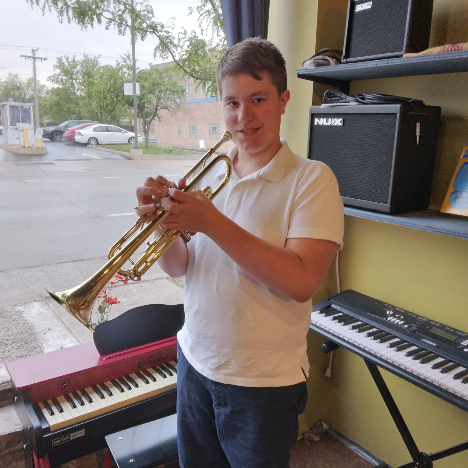boy student playing his trumpet in front of a couple electric pianos and amplifiers