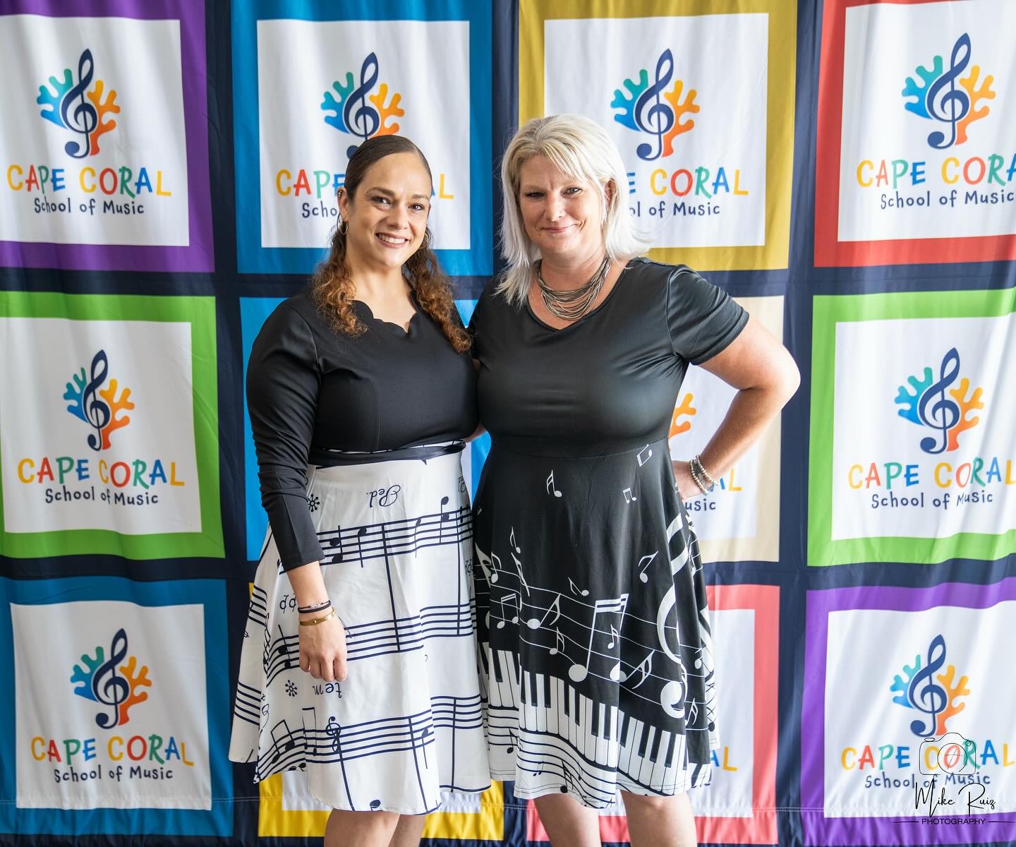 two of our managers standing in front of a step and repeat with a school logo on it