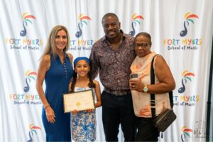 a student holding her certificate and standing with her parents and a grandparent in front of our step and repeat
