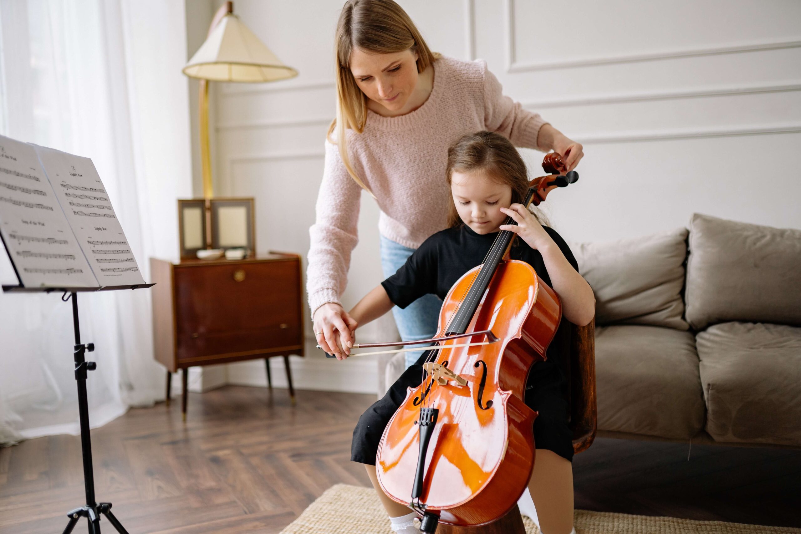 Woman helping young child learn cello