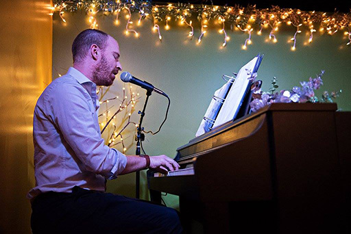Man playing piano and singing into microphone at Green Brooms Music Academy recital