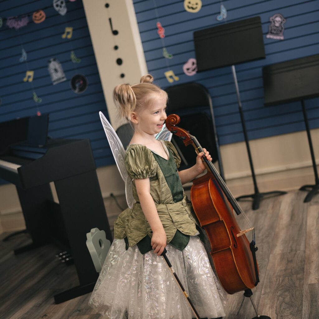 a little girl wearing a princess-fairy costume, holding a cello smiling after a performance