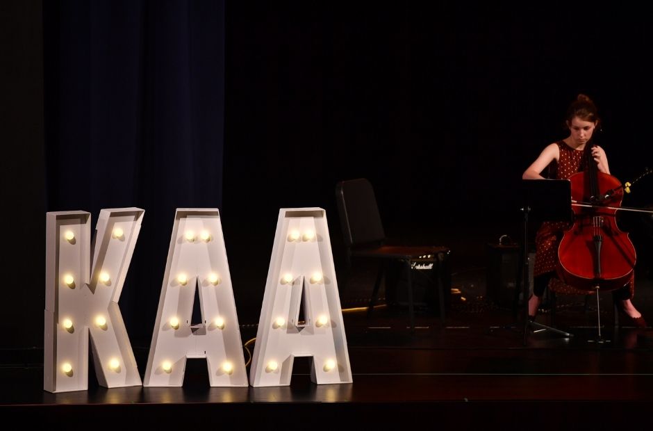 cello player perforing on stage next to a kentucky arts academy marquee 