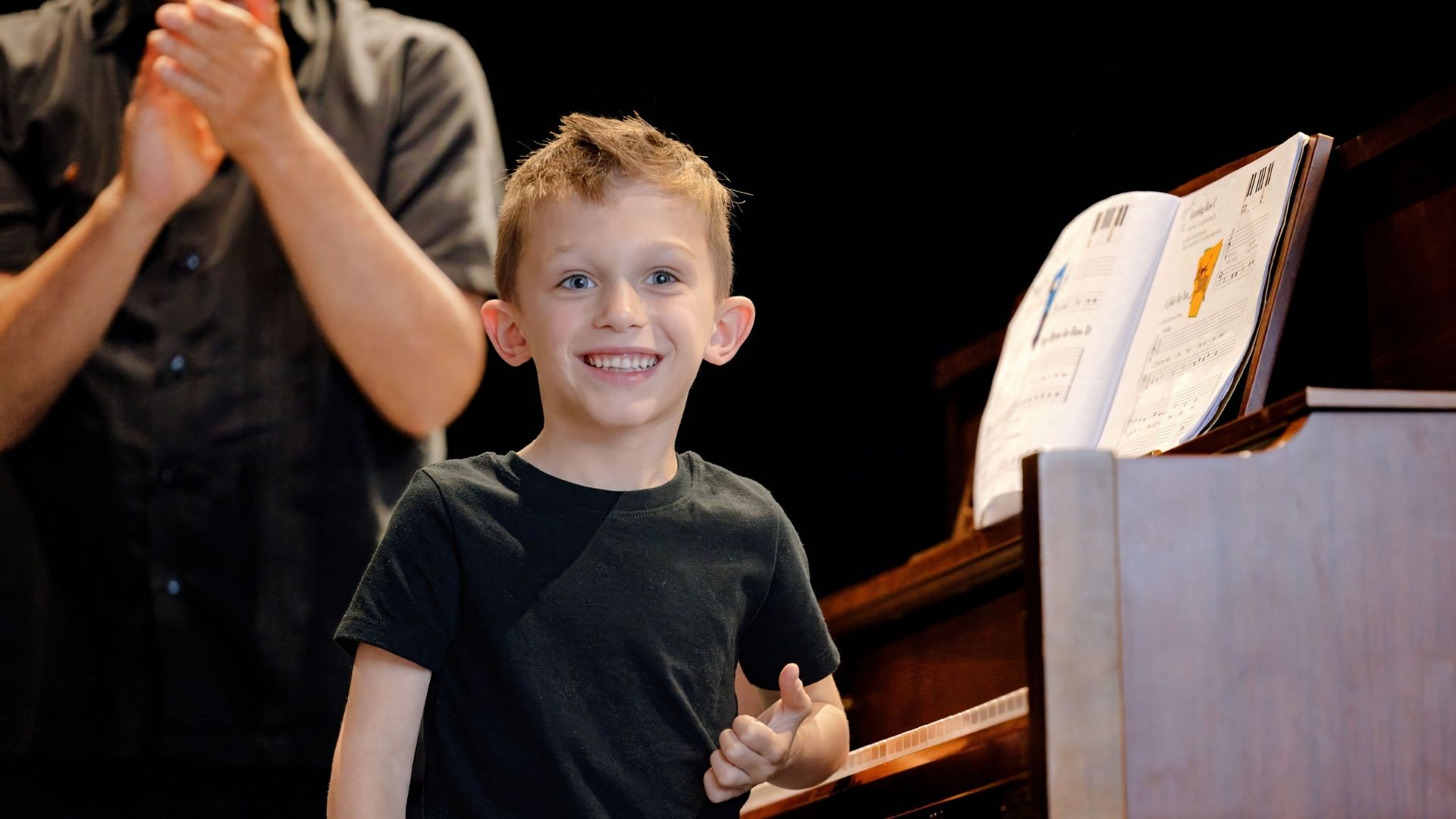 boy student smiling and standing in front of his piano after a performance