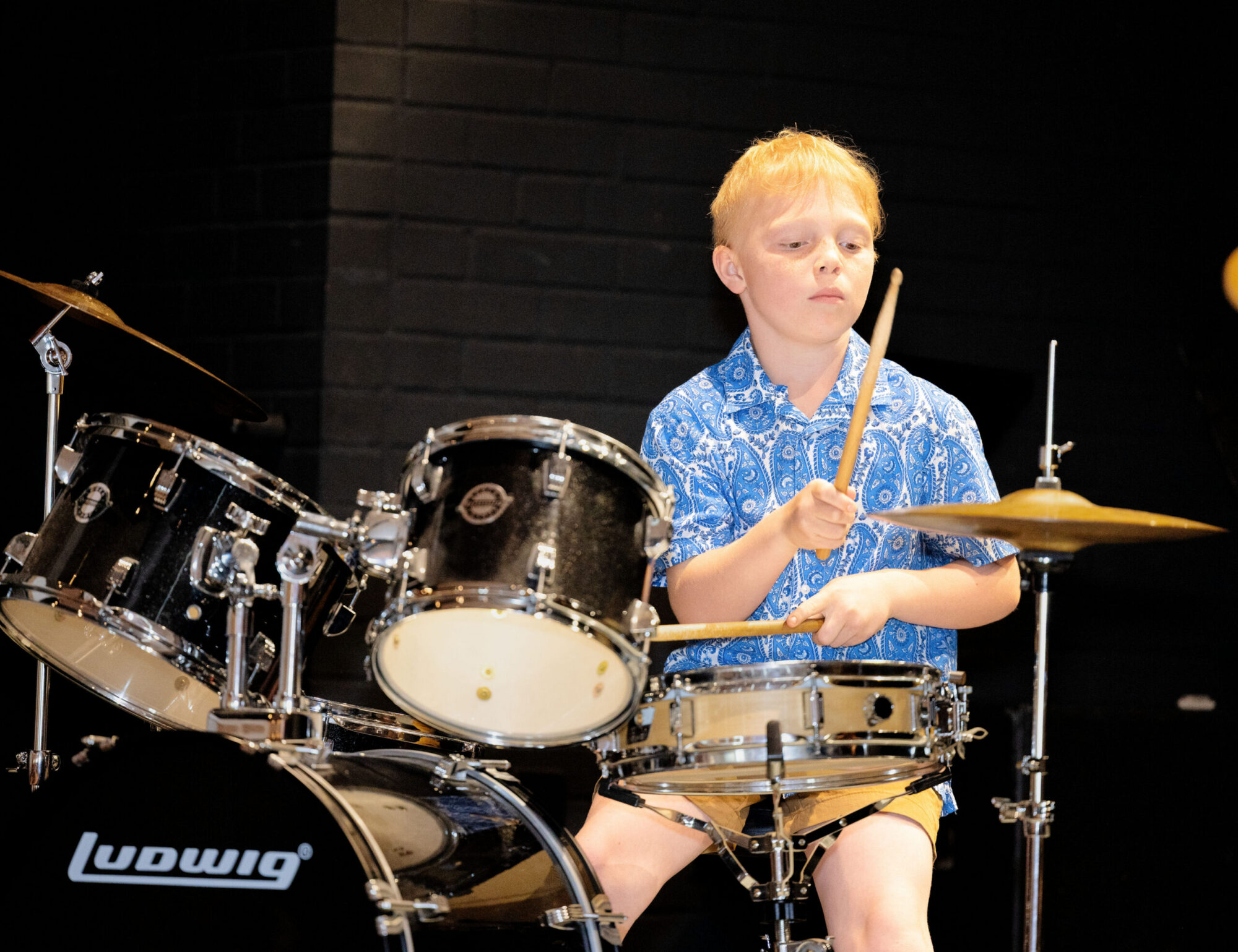 Blonde boy in a blue shirt playing the drums