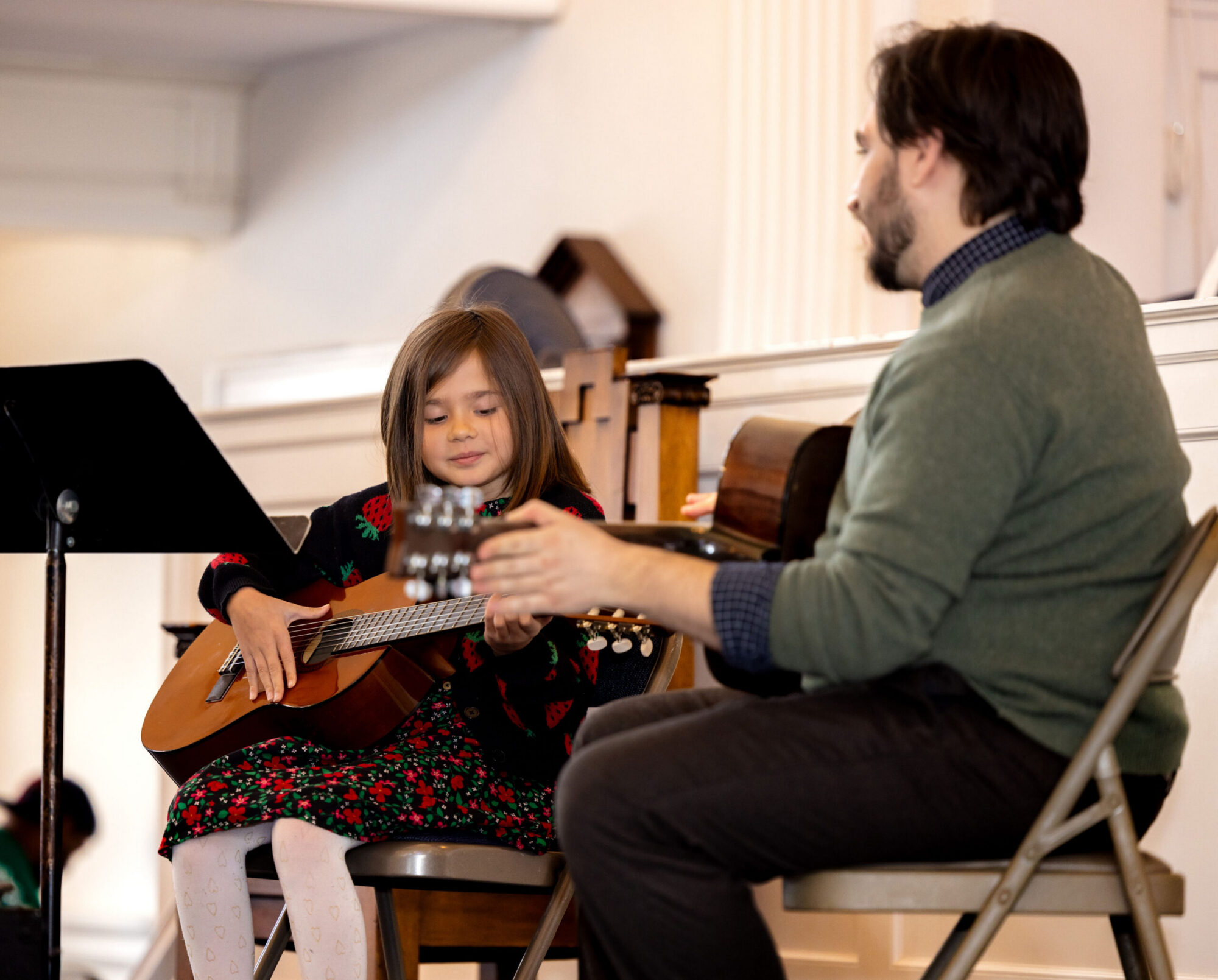 Little girl playing acoustic guitar with her teacher