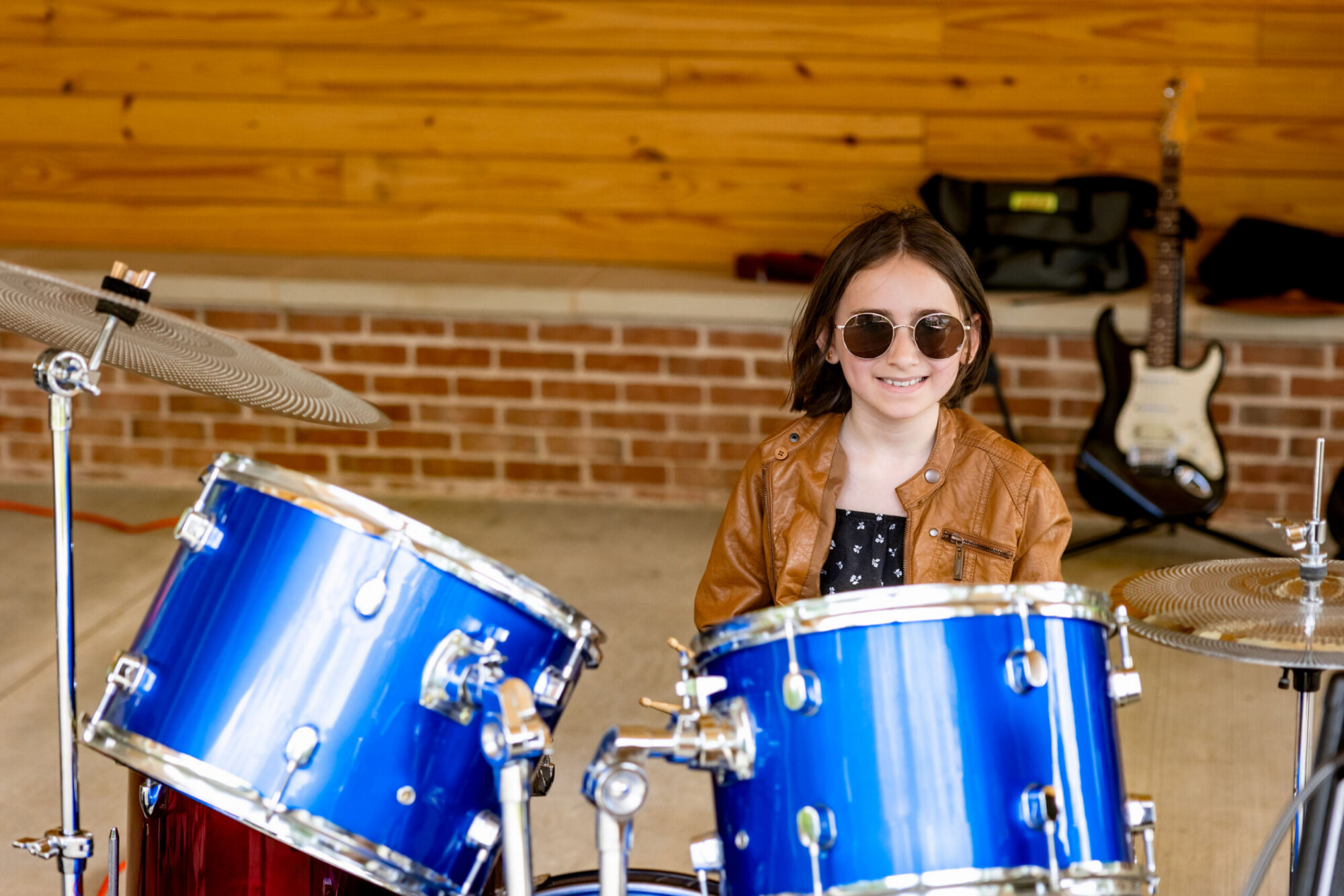 Girl wearing sunglasses sitting at a blue drum set