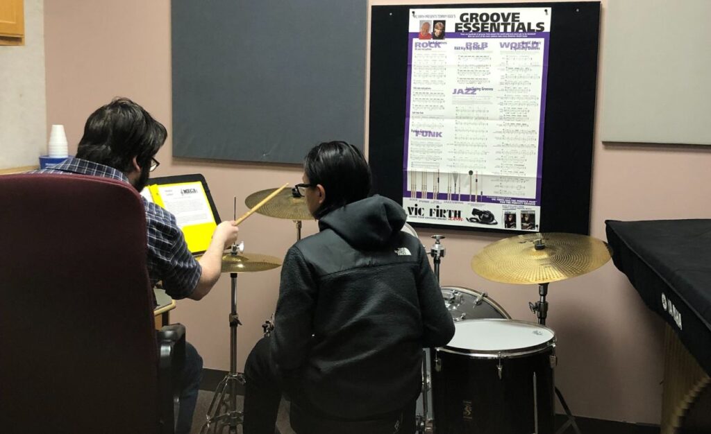 student learning to play the drums with a teacher