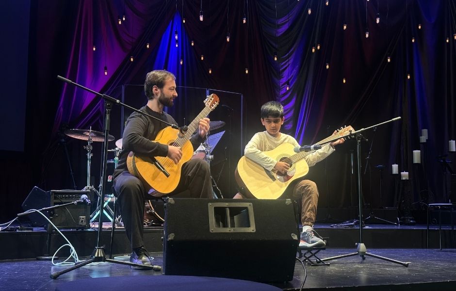 student and teacher playing guitar on stage