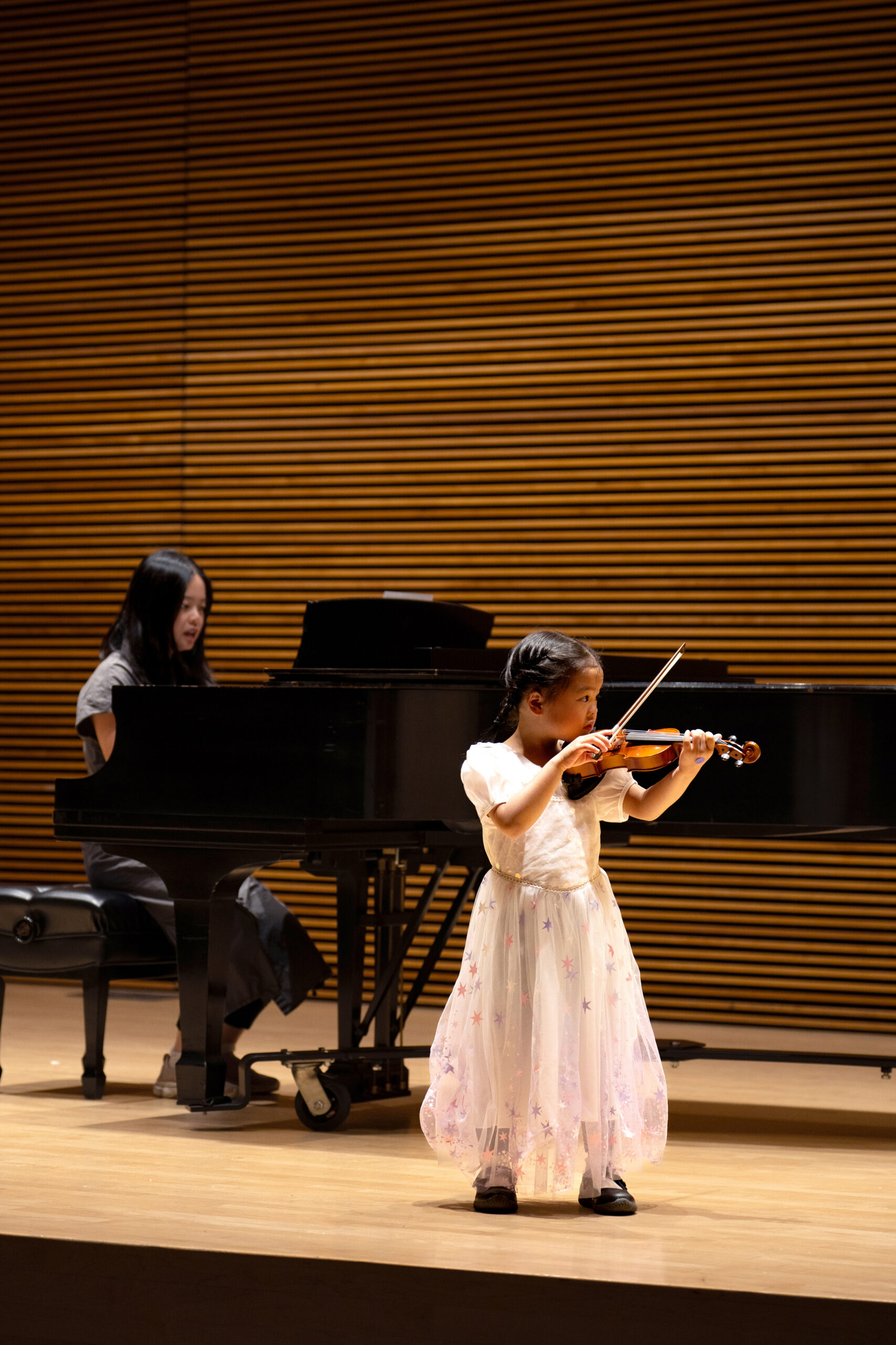 Little girl playing violin on stage with piano accompanist