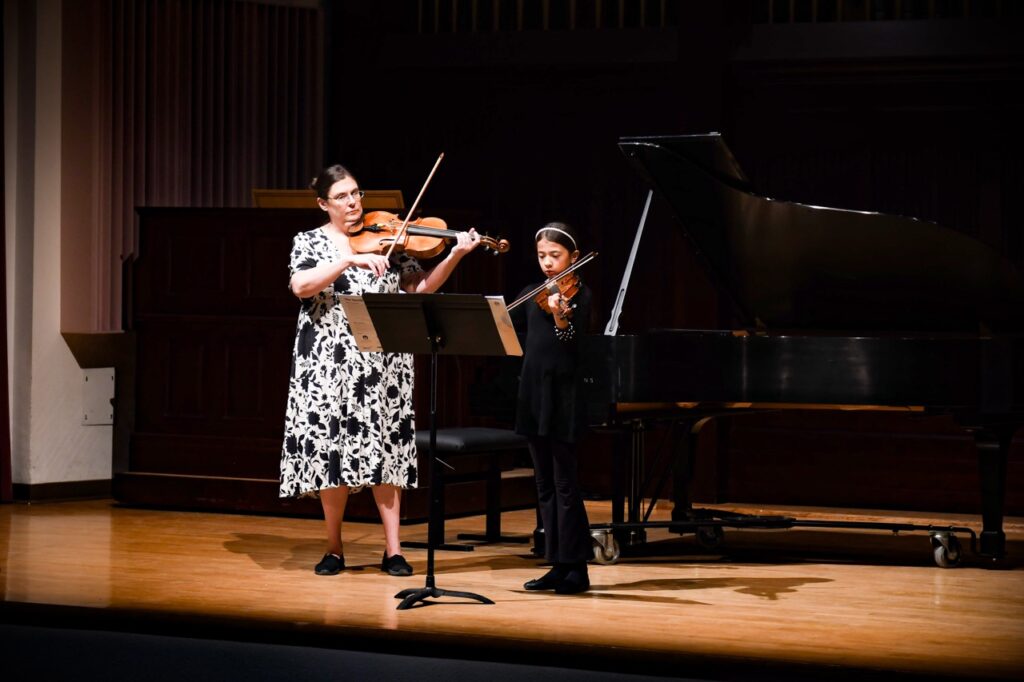 Young female violinist performing alongside instructor