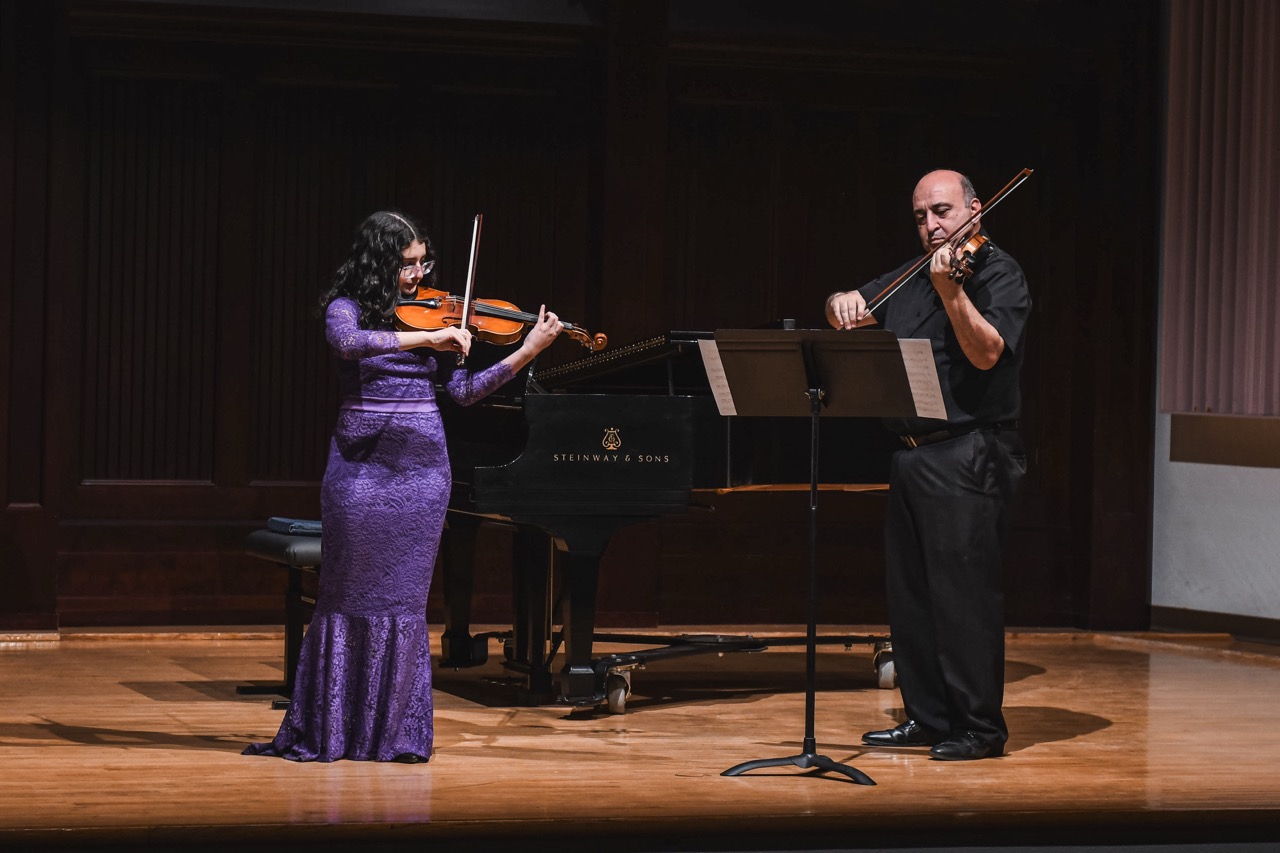 teacher and student playing violin on stage
