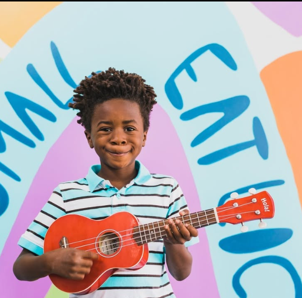 young boy playing red ukulele