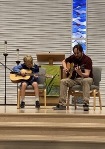 Teacher and student playing acoustic guitar on stage