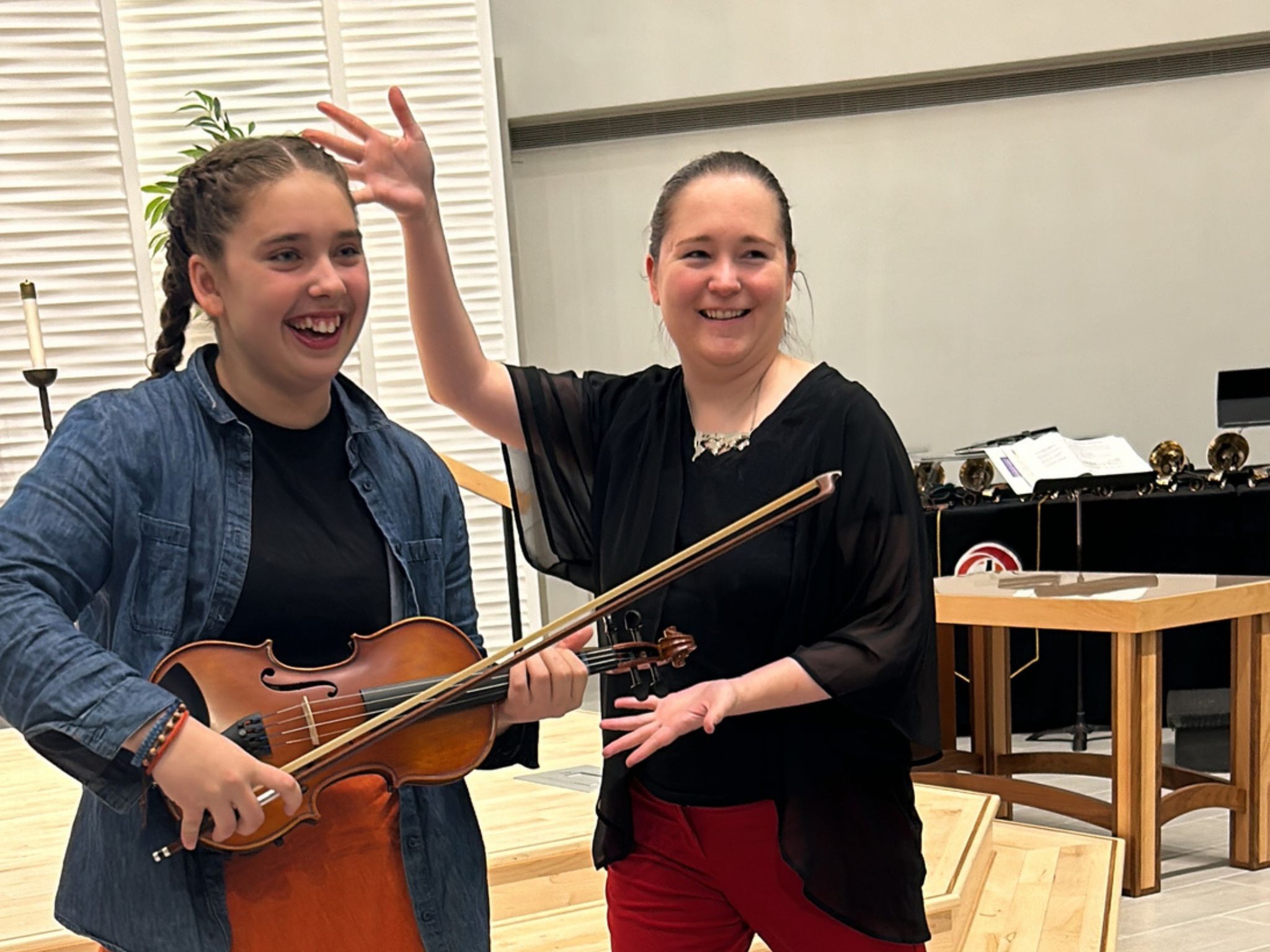 Girl with violin next to a woman giving jazz hands