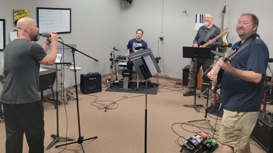 adult band in rehearsal with a vocalist, guitarist, bassist, and drummer