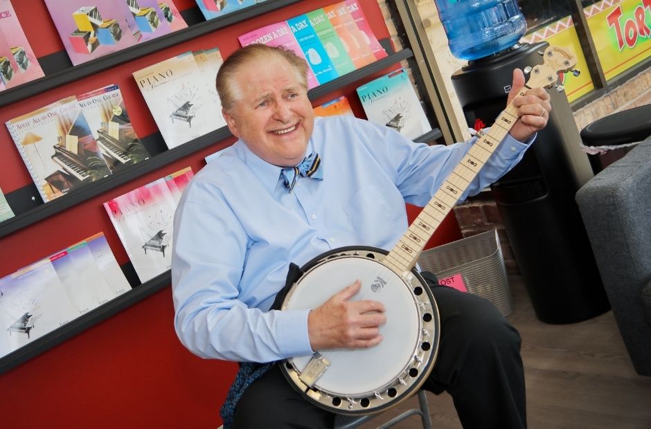 teacher in a blue shirt and bowtie playing a banjo in the school lobby