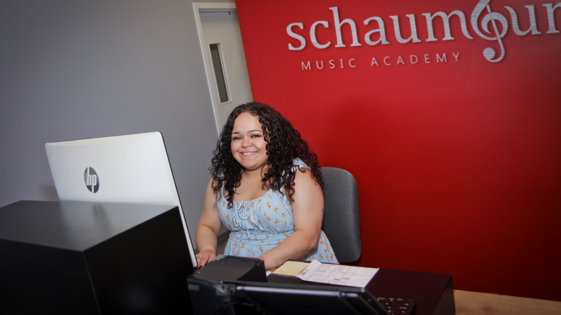 office admin sitting at the desk, working on the computer,  smiling at work against a red background