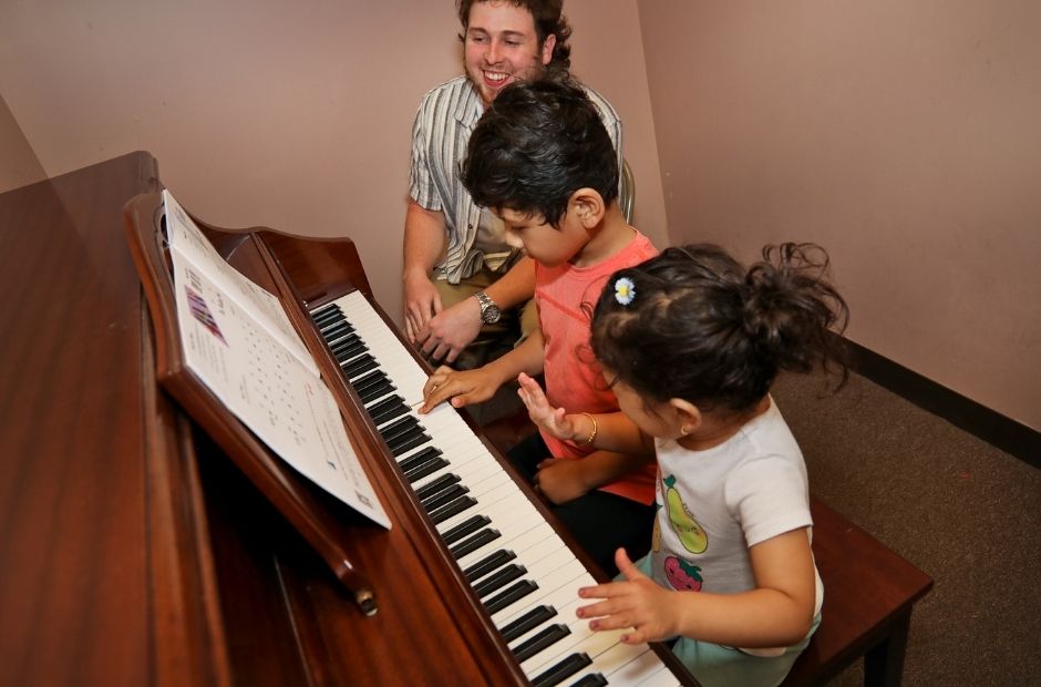 two young piano students and a piano instructor in a lesson