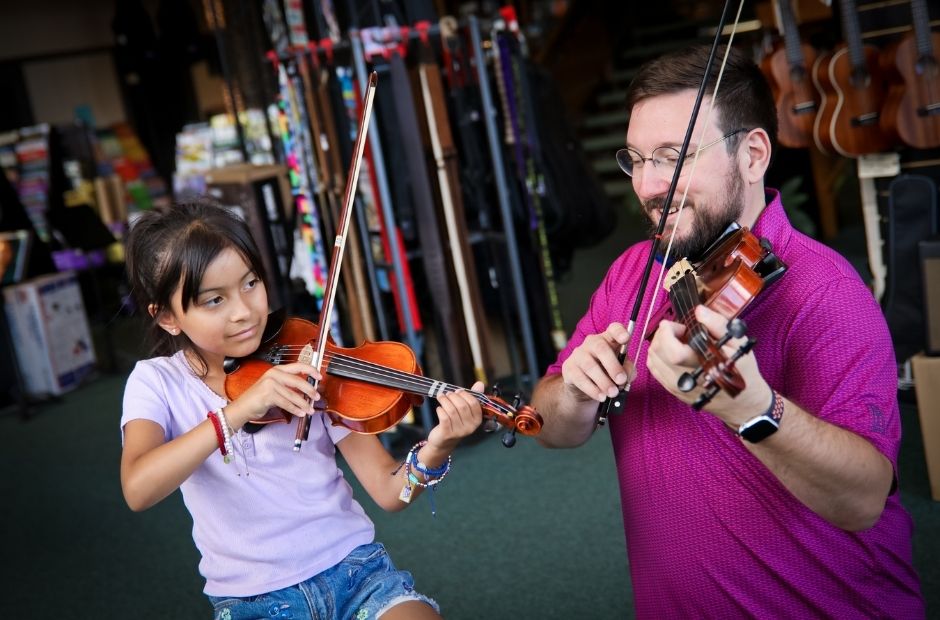 violin teacher and student playing their violins together in a music store lobby