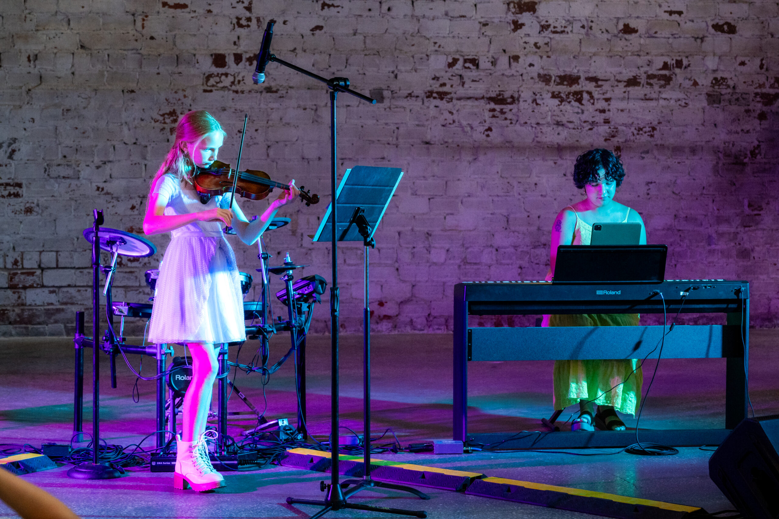 Girl on stage playing violin with teacher accompanying on piano