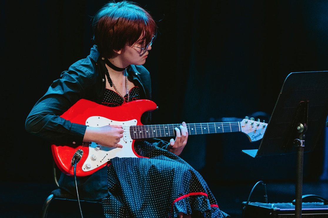 Student playing a red electric guitar