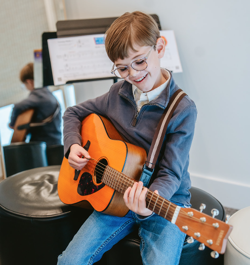 boy with glasses playing acoustic guitar