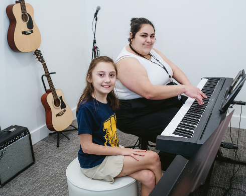 teacher and student in a piano lesson together, smiling at the camera