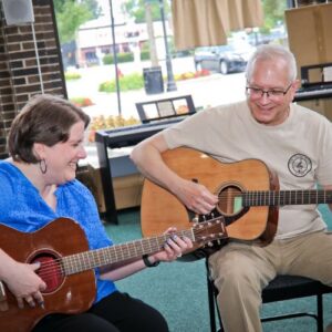 adult guitar student sitting and playing her instrument with her instructor