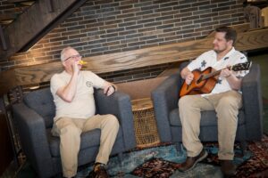 two instructors sitting in chairs playing their instruments, a kazoo and guitar, together.