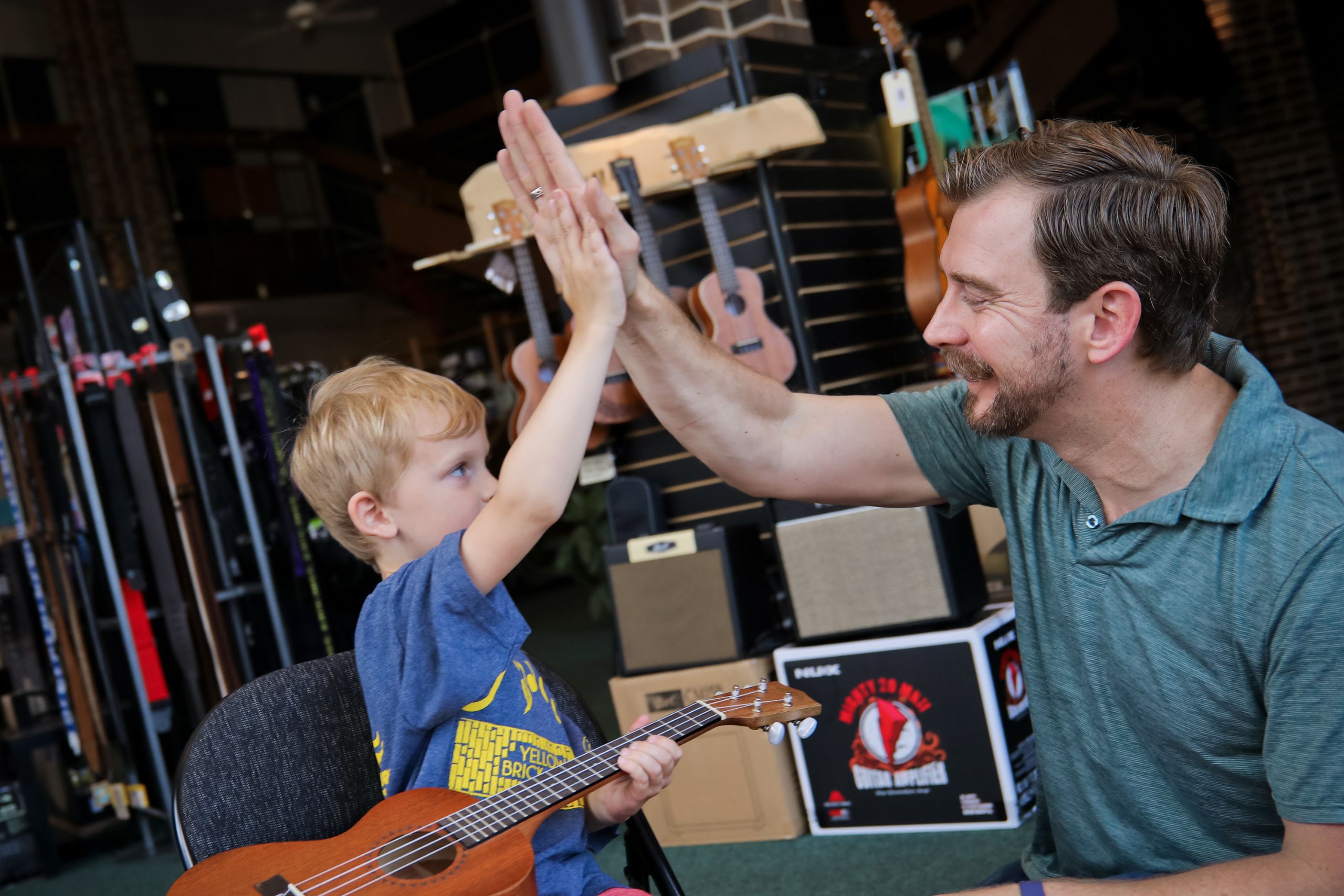 instructor giving a high five to his young ukulele student who is holding his ukulele