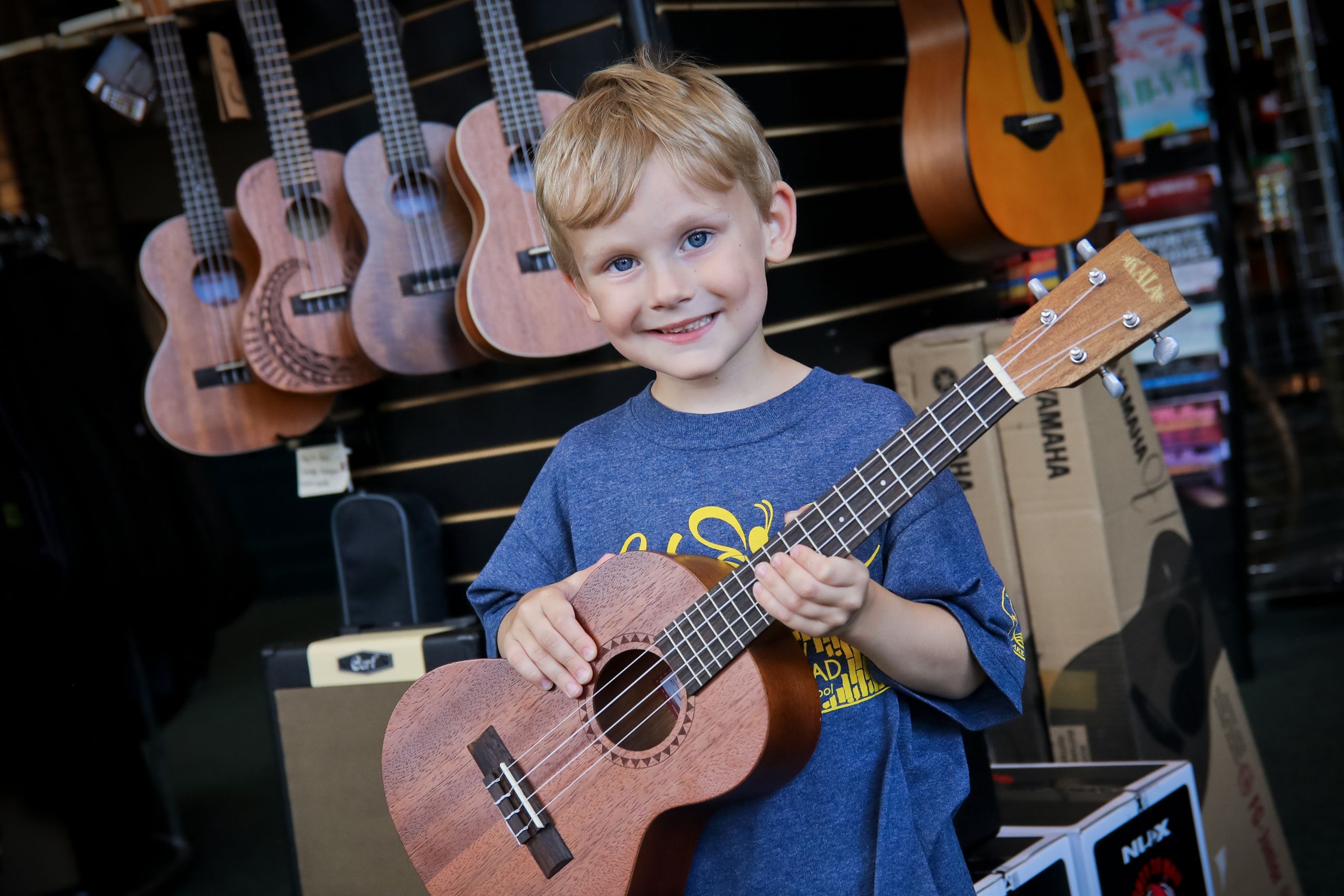 young boy with blonde hair and blue shirt holding a ukulele