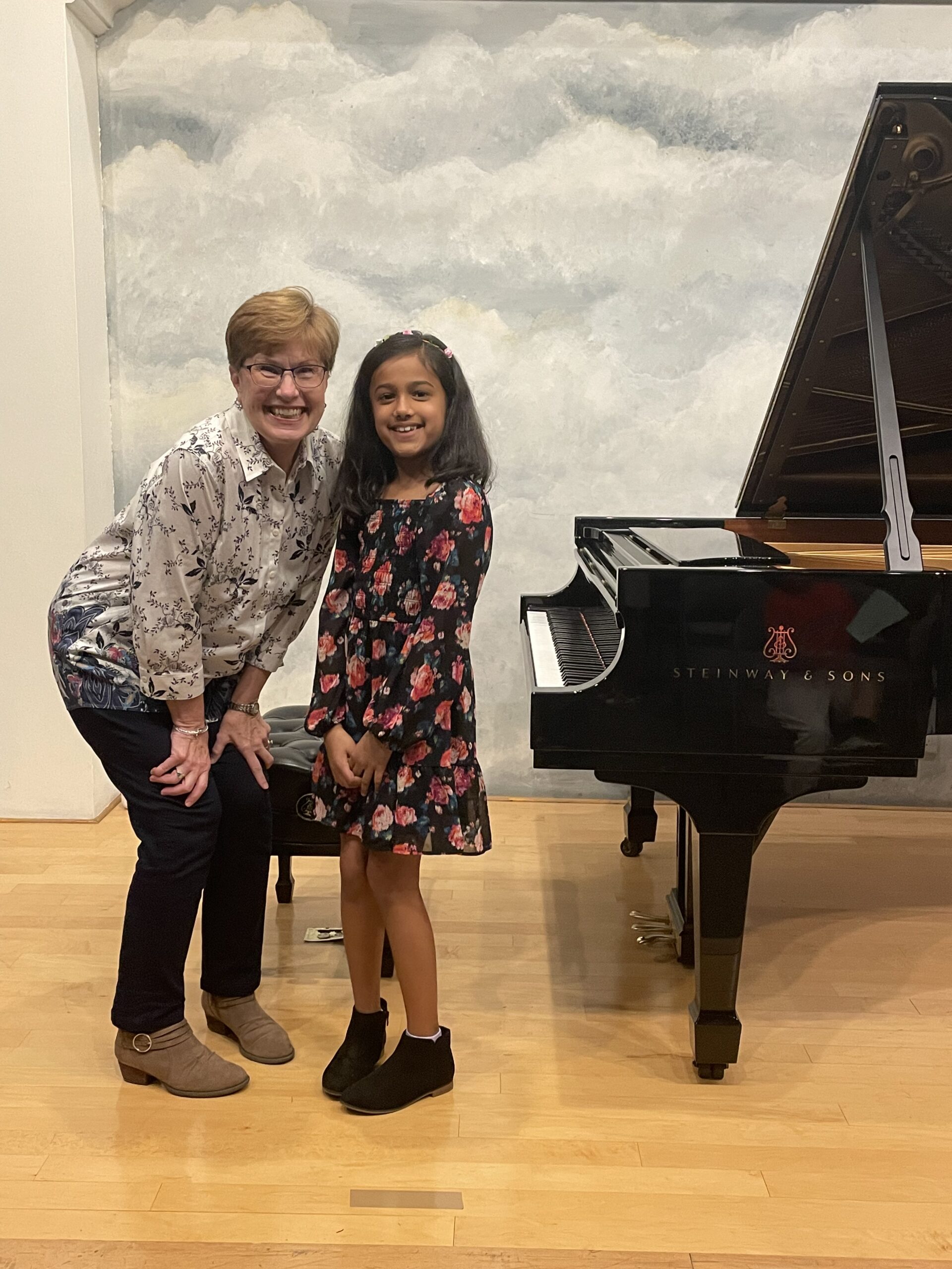 piano teacher and her student smiling after a performance on stage in front of their piano