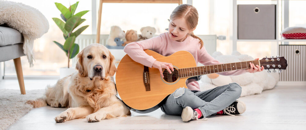 small girl playing guitar with dog next to her